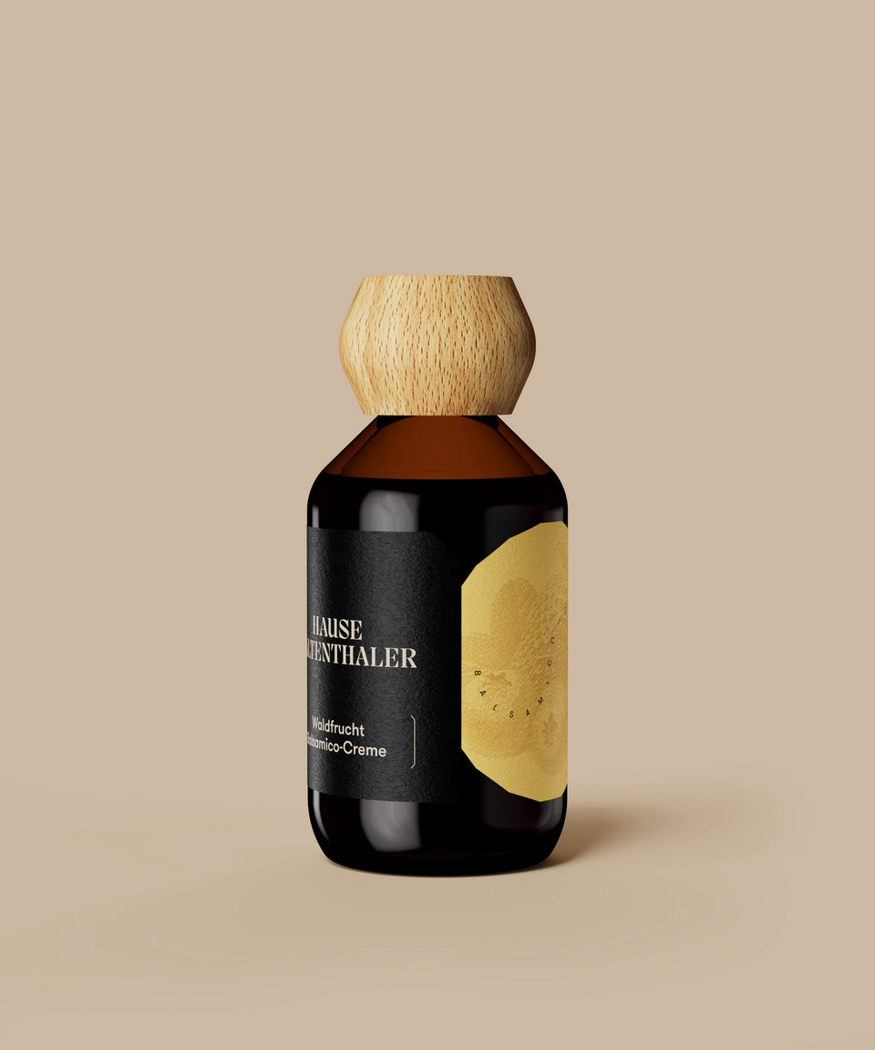 Braunglasgefäß mit Holzdeckel und schwarzem Etikett mit einer goldenen Fruchtillustration der WALDFRUCHT-BALSAMICOCREME von Hause Kaltenthaler auf beigem Hintergrund.