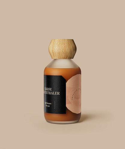 Eine braune Glasflasche mit Holzkappe und schwarzem Etikett vor einem beigen Hintergrund - perfekt für die Präsentation von Haus Kaltenthaler APRIKOSEN SHRUB.