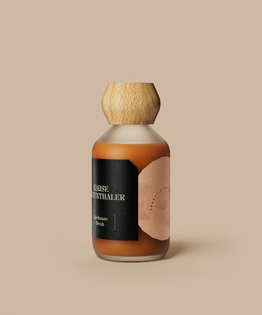 Eine braune Glasflasche mit Holzkappe und schwarzem Etikett vor einem beigen Hintergrund - perfekt für die Präsentation von Haus Kaltenthaler APRIKOSEN SHRUB.