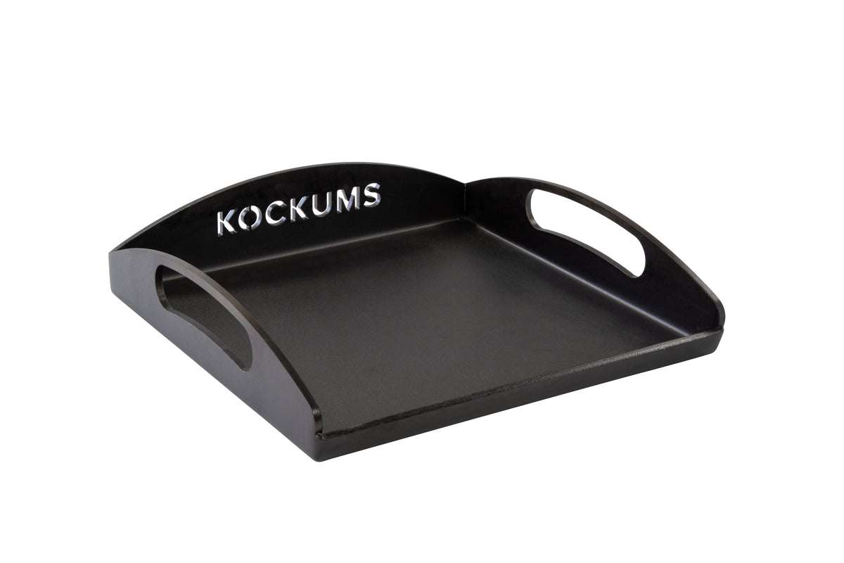 Die GRIDDLEPLATTE KOCKUMS 35 X 35 CM von Kockums Jernverk ist ein schwarzes Tablett aus schwedischem Kohlenstoffstahl mit ausgeschnittenen Griffen und dem „Kockums“-Logo auf der erhöhten hinteren Kante.