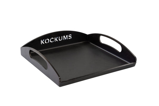 Die GRIDDLEPLATTE KOCKUMS 35 X 35 CM von Kockums Jernverk ist ein schwarzes Tablett aus schwedischem Kohlenstoffstahl mit ausgeschnittenen Griffen und dem „Kockums“-Logo auf der erhöhten hinteren Kante.