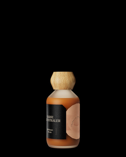In einer Glasflasche mit Holzkappe und schwarzem Etikett befindet sich der Haus Kaltenthaler APRIKOSEN SHRUB, ein bernsteinfarbener Fruchtmarkbalsamico mit feiner Balsamicosäure, der sich vor einem schwarzen Hintergrund präsentiert.