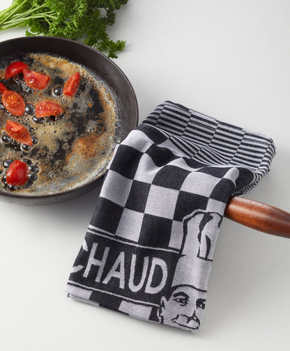 Eine Bratpfanne mit Essen steht neben einem schwarz-weiß karierten Le Chaud devant PREMIUM KÜCHENTUCH - PROFIKÜCHEN-TORCHON, der über den Griff drapiert ist, und frische Petersilie verleiht der Arbeitsplatte einen Hauch von Grün.