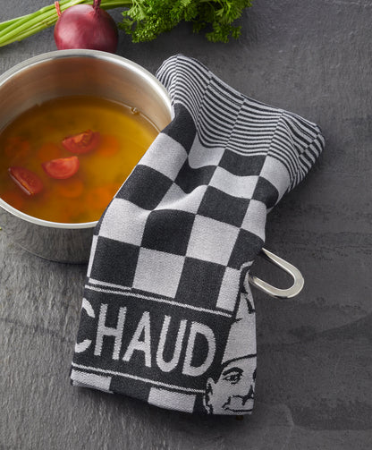 Ein Topf Suppe mit Tomaten, teilweise bedeckt mit einem karierten PREMIUM KÜCHENTUCH von Le Chaud devant, steht neben frischen Kräutern und einer roten Zwiebel.